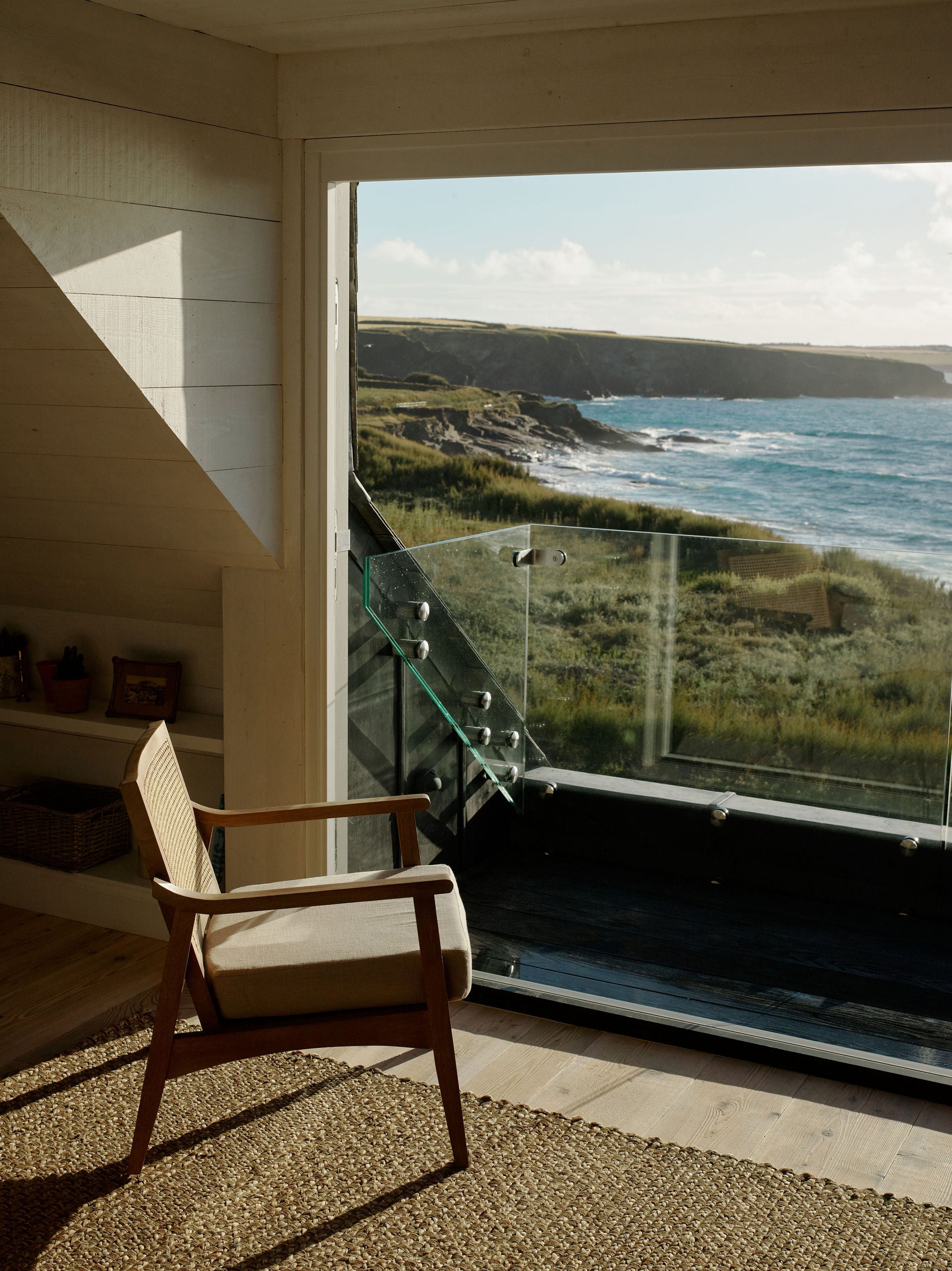 Golden hour sun hitting art deco reading chair with a view out to sea from a large window balcony.