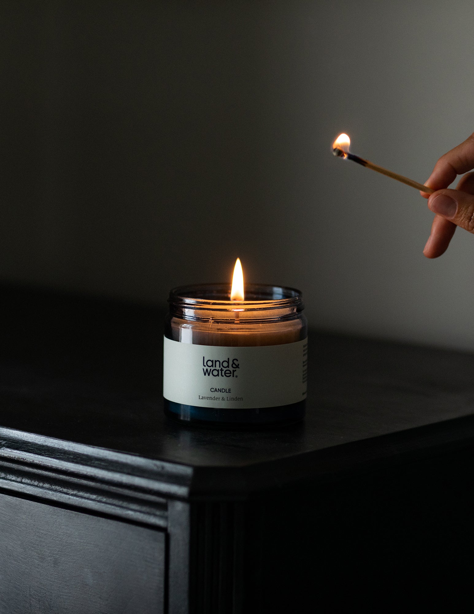A person with a match after lighting a land&water candle on top of a bedside table