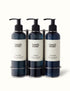 A brushed stainless steel triple wall bracket with three black pump bottles labeled &