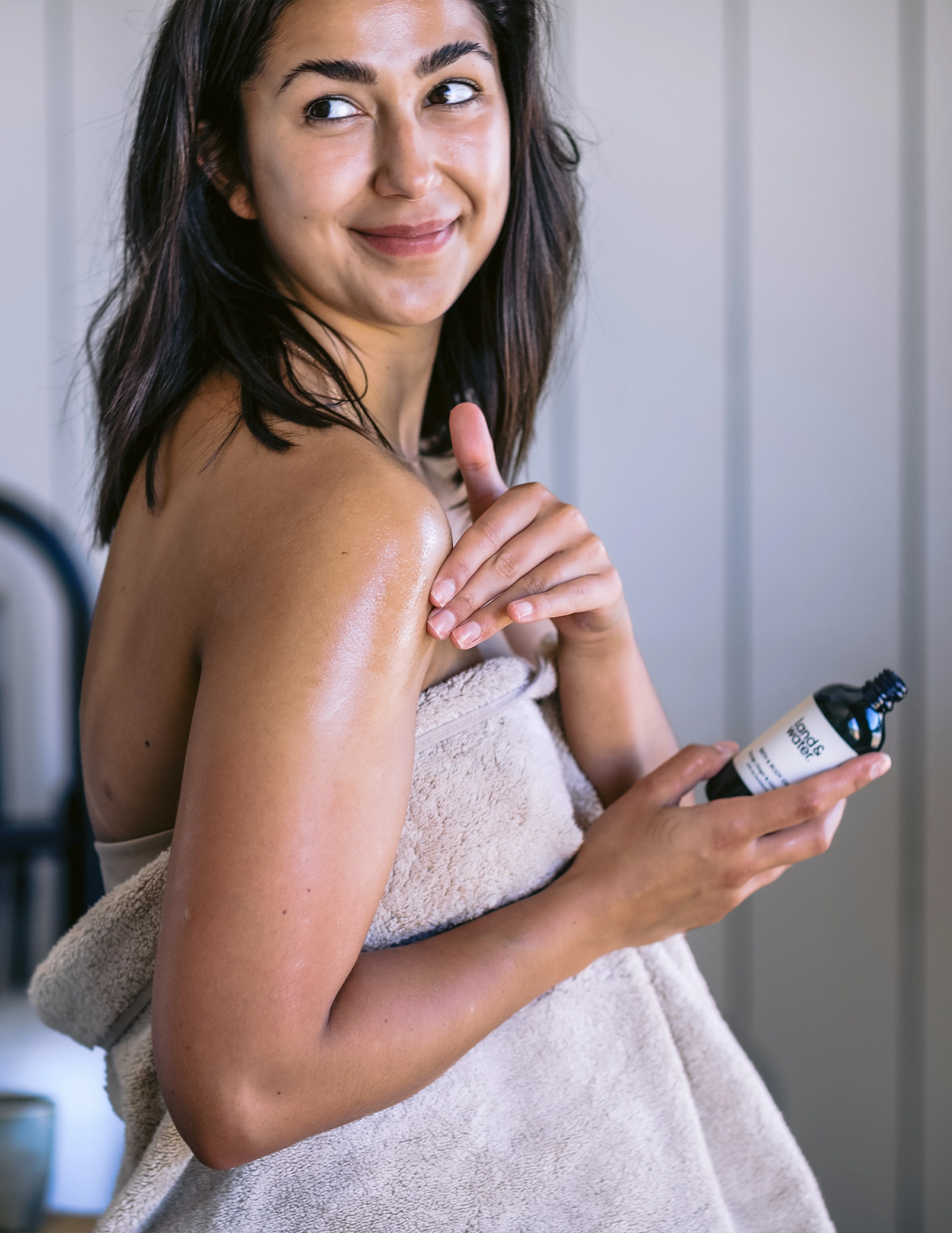 Woman wrapped in towel smiling and holding bottle