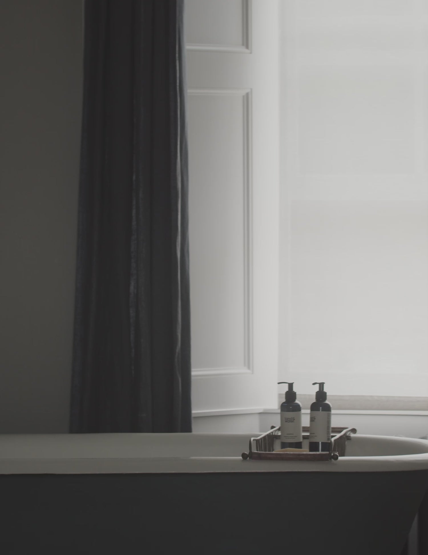 A short film clip in a bathroom setting, with land&water bottles on a bath rack over the bath. A woman is in the bath washing her hair with land&water shampoo.