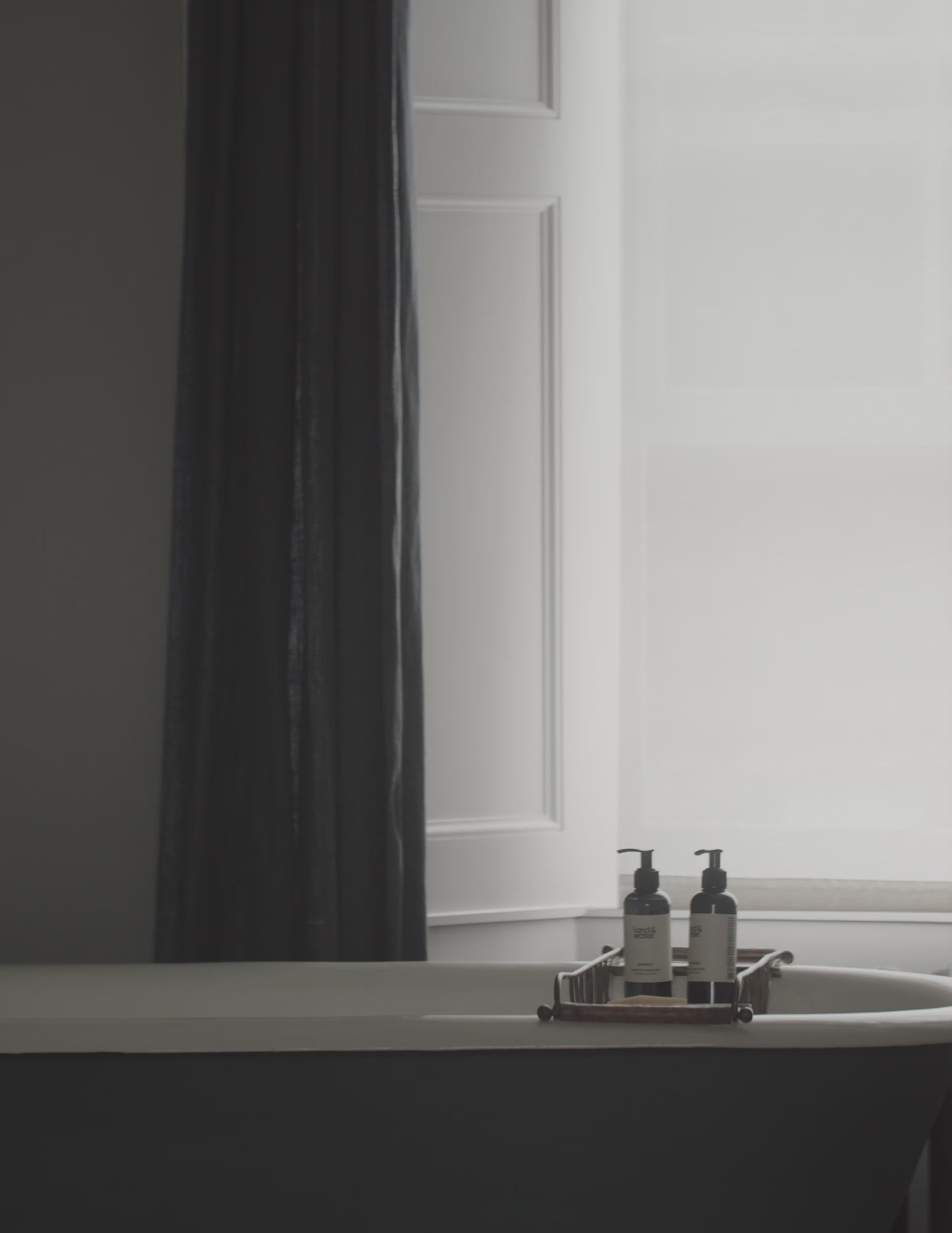A short film clip in a bathroom setting, with land&water bottles on a bath rack over the bath. A woman is in the bath washing her hair with land&water shampoo.