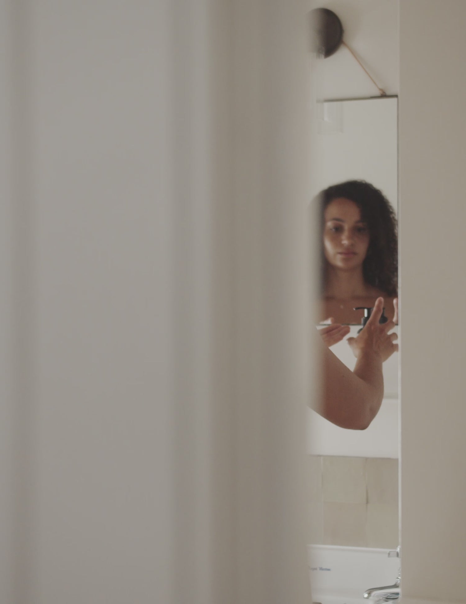 A short film clip of a woman wrapped in a towel rubbing land&water body lotion into her skin around her neck and shoulders.