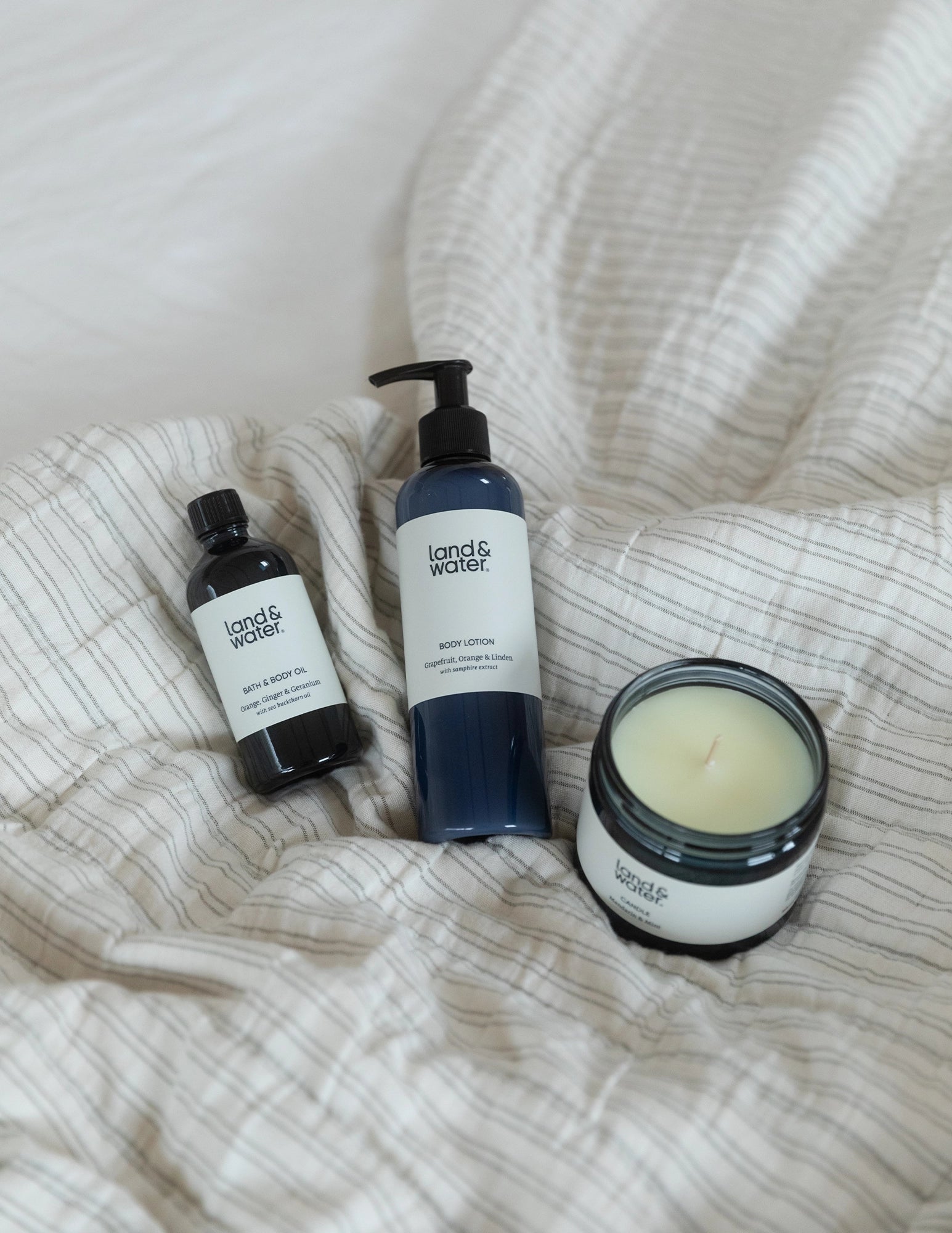 A bath & body oil bottle, body lotion and mandarin and mint candle on a bed cover.