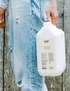 A person wearing blue jeans holding a large 5L bottle of alcohol hand gel.