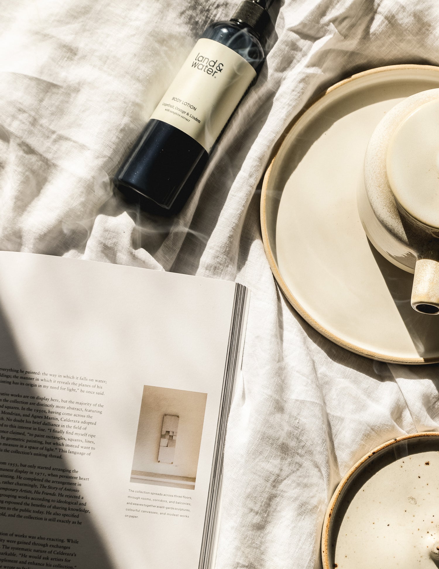 A bottle of body lotion placed on a flat surface with a magazine and ceramic plates, providing a soothing and natural aesthetic.