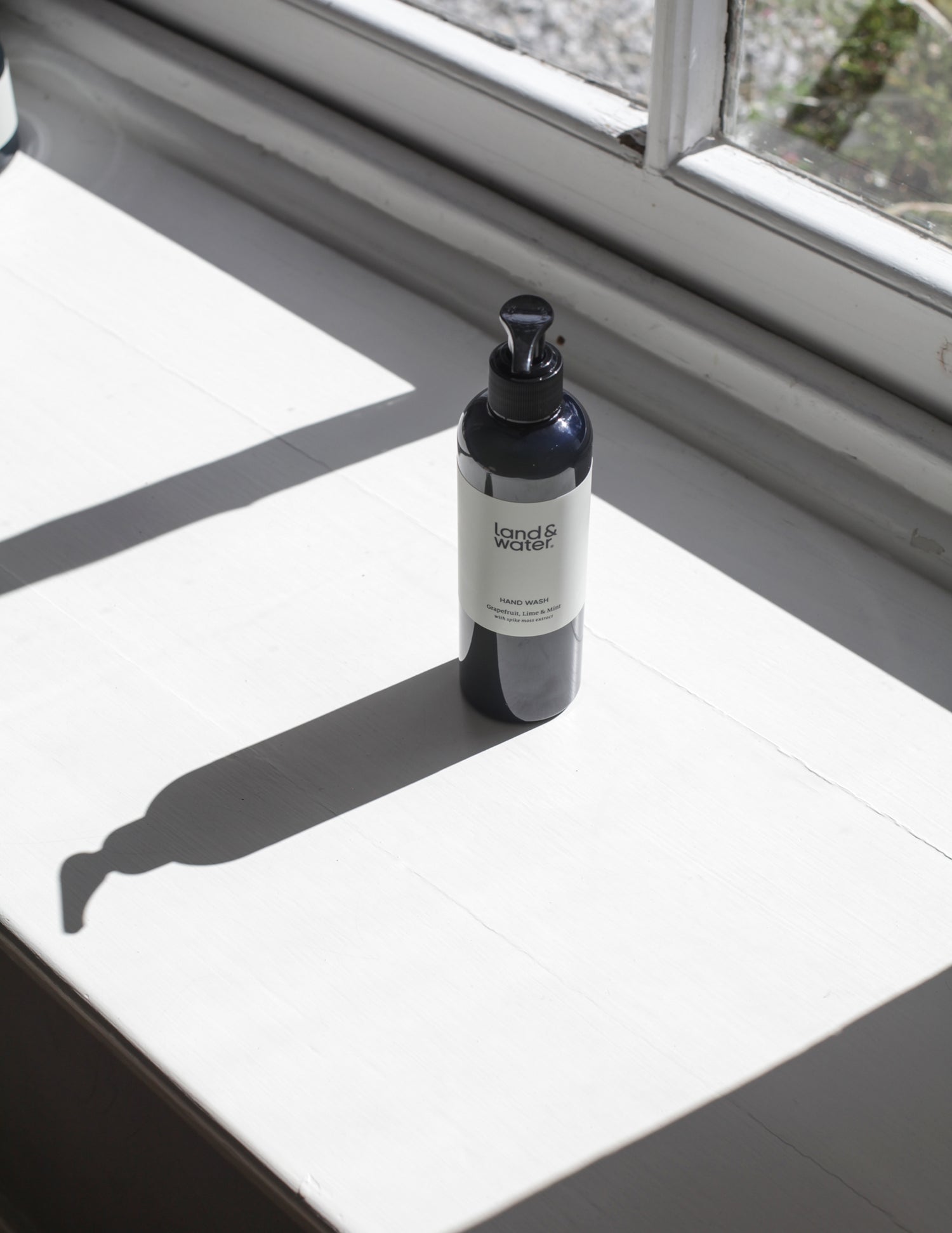 A land&water hand wash bottle on a sunny windowsill.