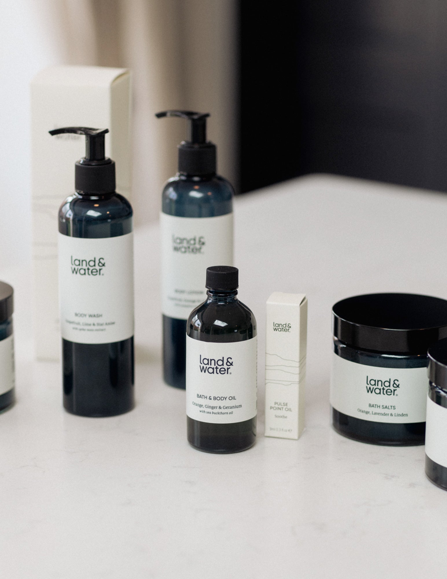 A collection of bath and body products from the brand Land & Water, including bottles, jars, and a candle, displayed on a white surface with packaging visible.