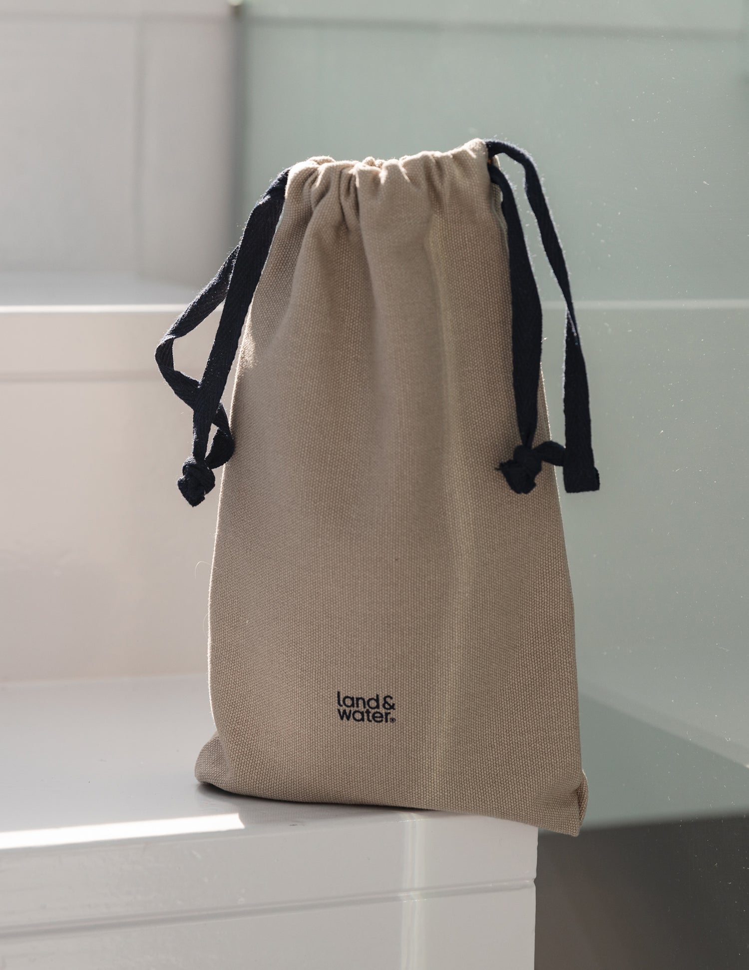 A large, beige, cotton drawstring bag with land&water on the front, placed on a white staircase
