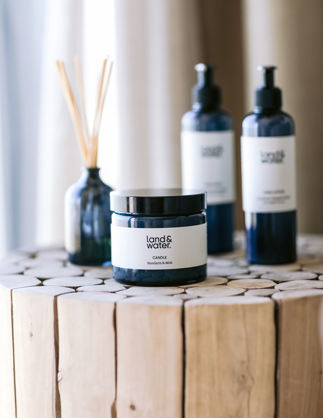 A set of home fragrance products including a candle, hand wash, hand lotion, and a reed diffuser presented on a wooden surface.