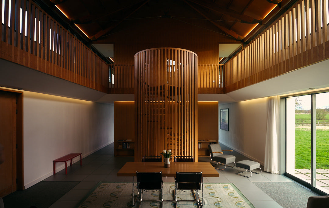 Wide lens image of Long House interior living space featuring spiral wooden staircase. Living Architecture