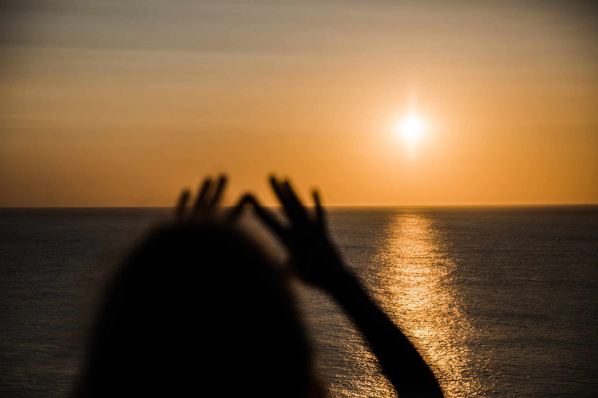 Sunset photograph of someone holding out thier hands to the ocean horizon.